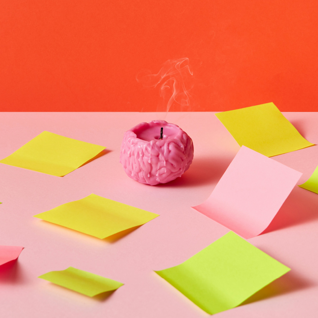 A melting, brain-shaped candle on a pink desk, surrounded by yellow and pink post-it notes