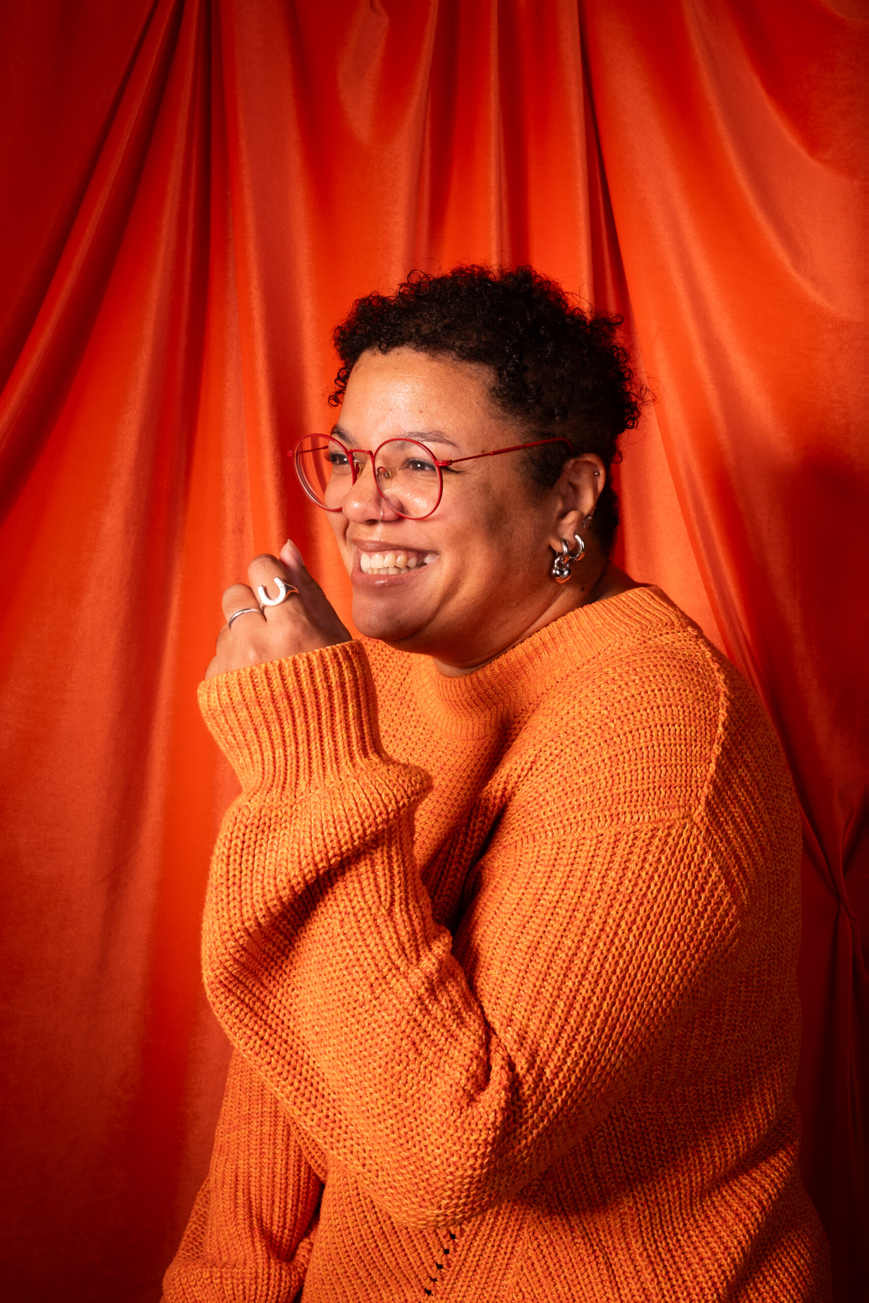 Studio shot of Yvie Ormsby, founder of Yoco Studio. She's wearing a cozy orange jumper and caught mid-laugh.