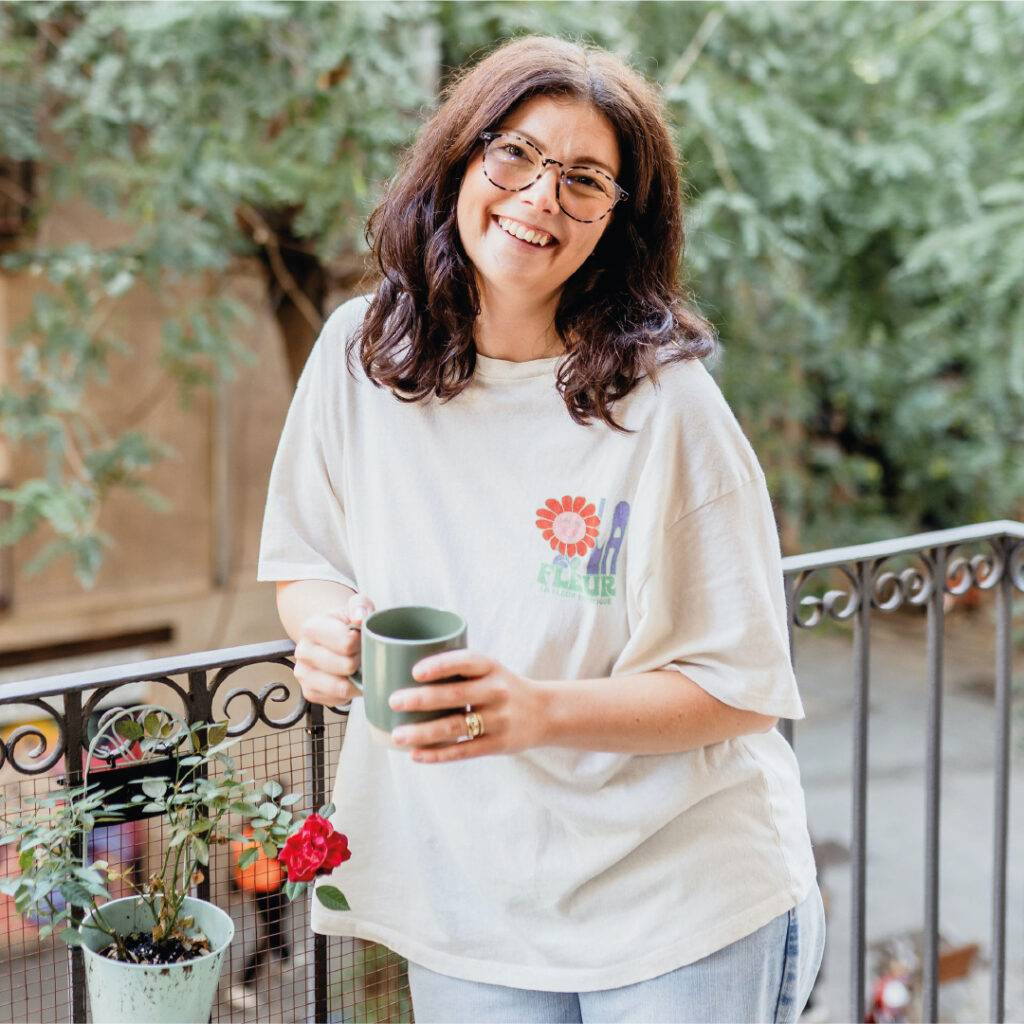 Laura Blume (Thought Partner & Coach) leaning against a wrought-iron fence